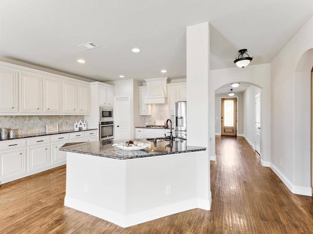 1020 Fallon Drive, McKinney, TX 75071 Kitchen featuring white cabinetry, dark stone countertops, an integrated stainless steel oven, and wood-finish flooring