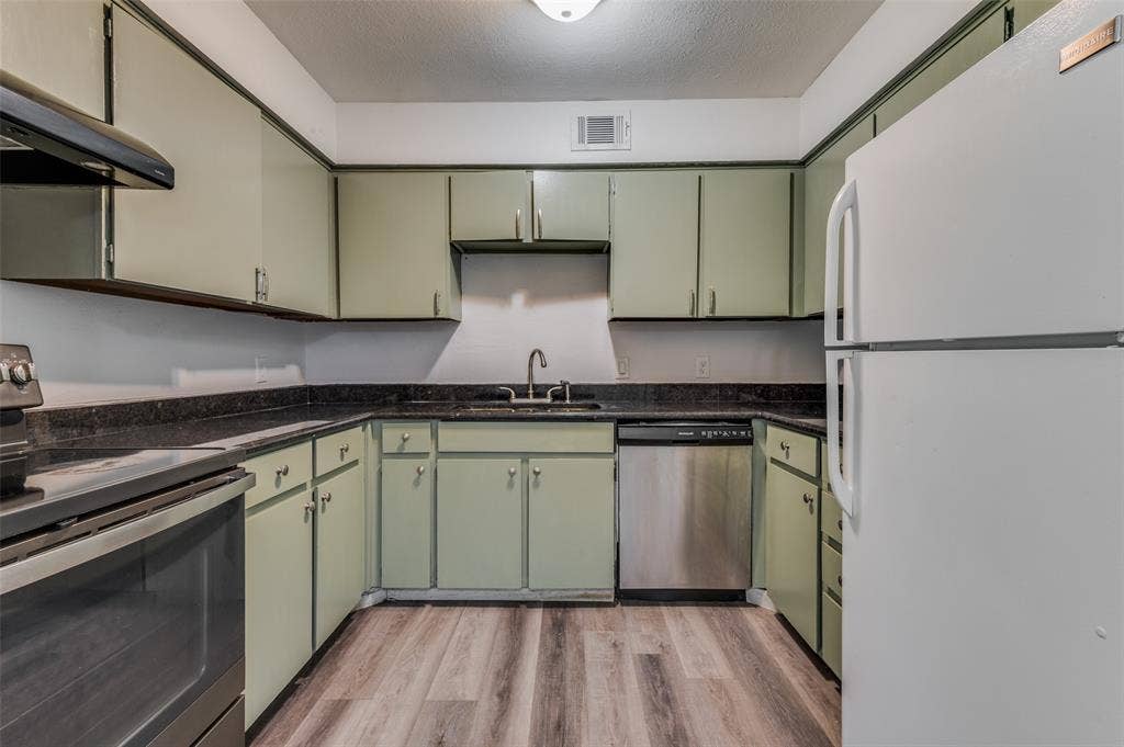 428 N Dallas Avenue, #3, Lancaster, TX 75146 U-shaped kitchen featuring light green cabinetry, dark countertops, wood-finish flooring, and stainless steel dishwasher