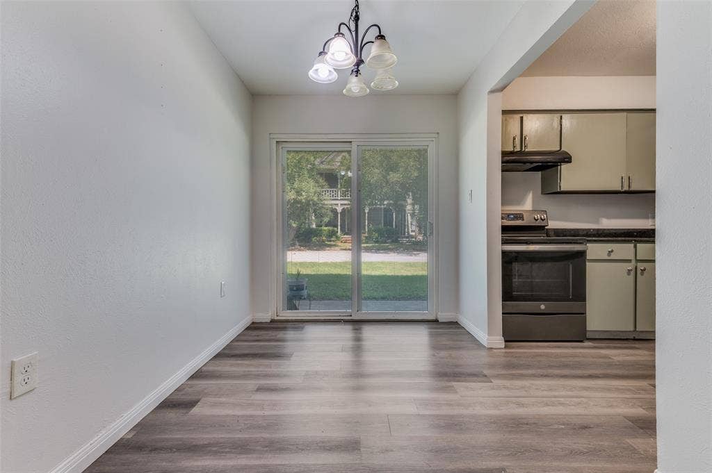 428 N Dallas Avenue, #3, Lancaster, TX 75146 Open concept living space featuring wood-finish flooring, abundant natural light from glass sliding doors overlooking the landscaped grounds, a contemporary pendant light fixture, and an adjacent kitchen with stainless steel appliances and neutral cabinetry
