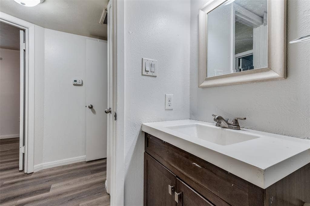 428 N Dallas Avenue, #3, Lancaster, TX 75146 Wood-finish flooring, white walls, dark wood-finish vanity with an integrated sink, silver-finish faucet, and a framed mirror