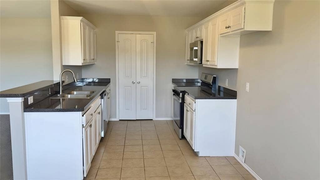 Kitchen featuring white cabinetry, dark countertops, a stainless steel sink, stainless steel appliances, and tile flooring