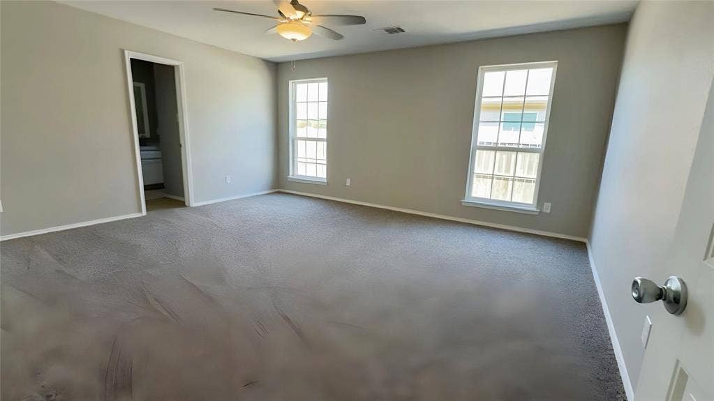 Spacious room featuring neutral carpeting, light gray wall paint, and a ceiling fan with integrated lighting