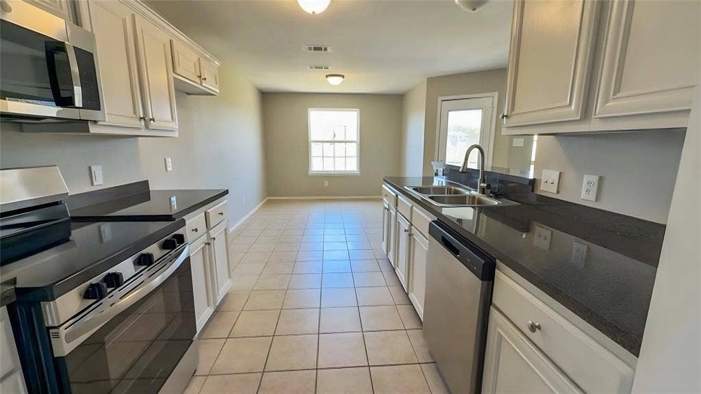 Kitchen featuring white cabinetry, dark countertops, stainless steel appliances, and tile flooring