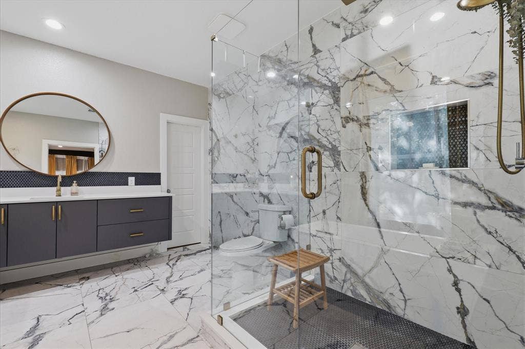 709 Woodbine Avenue, Dallas, TX 75203 Spacious bathroom featuring a floating vanity with dark cabinetry, a frameless glass shower enclosure, and large format marble-look tile flooring