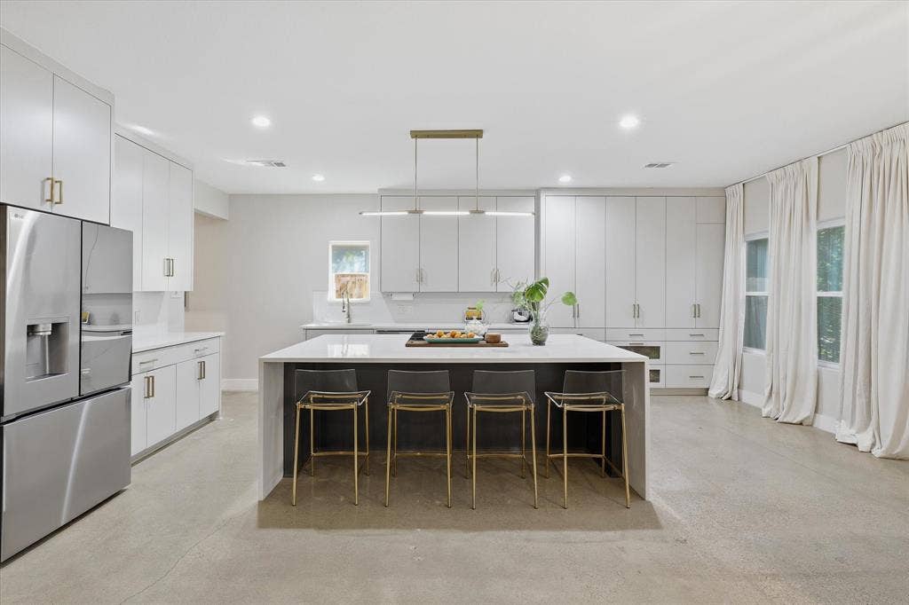 709 Woodbine Avenue, Dallas, TX 75203 Sleek kitchen featuring an expansive central island with a waterfall edge, stainless steel refrigerator, abundant white cabinetry with gold-tone hardware, and recessed lighting