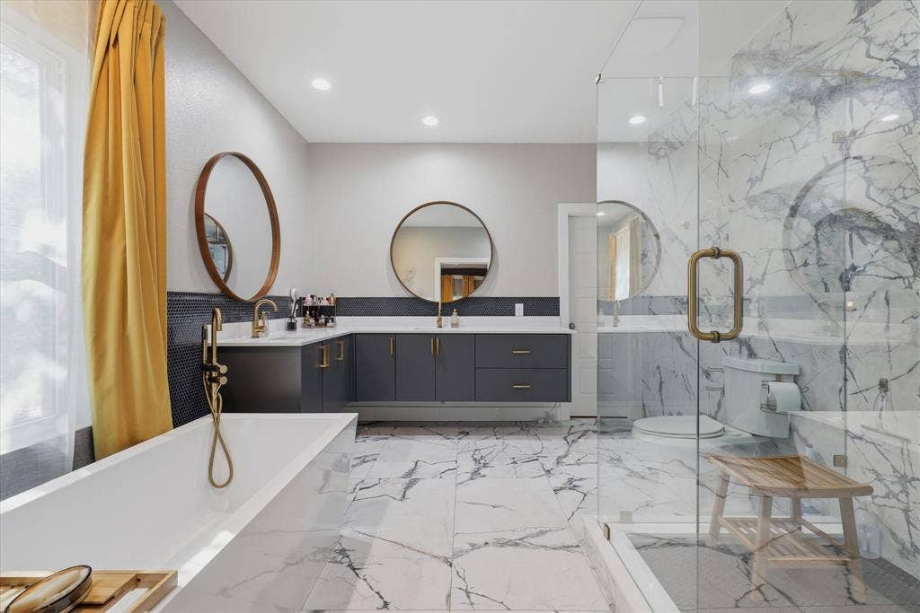 709 Woodbine Avenue, Dallas, TX 75203 Dual vanity with integrated sinks, freestanding soaking tub, glass-enclosed shower, gold-finish fixtures, and marble-look flooring