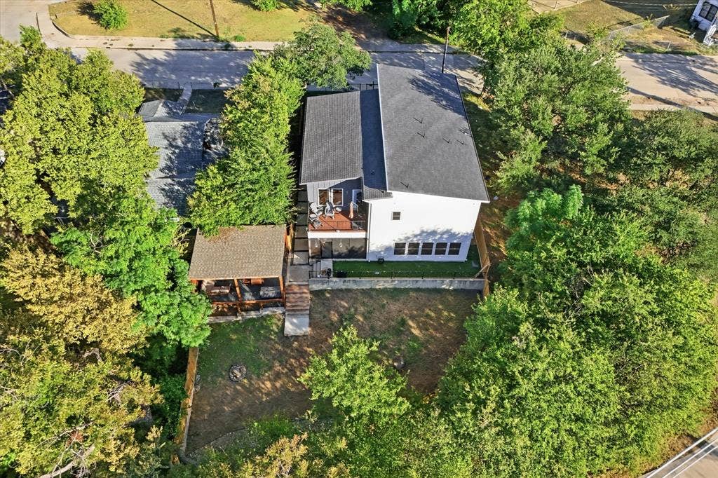 709 Woodbine Avenue, Dallas, TX 75203 Contemporary residential structure featuring a gray shingle roof, a second-story balcony with railings, a covered outdoor structure, and a fenced yard