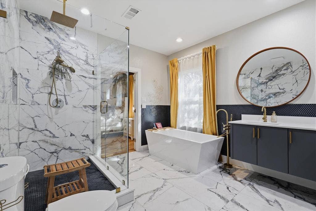 709 Woodbine Avenue, Dallas, TX 75203 Walk-in shower with clear glass enclosure and rainfall showerhead, freestanding soaking tub with floor-mounted faucet, dual-sink vanity with quartz countertop, and large round mirror