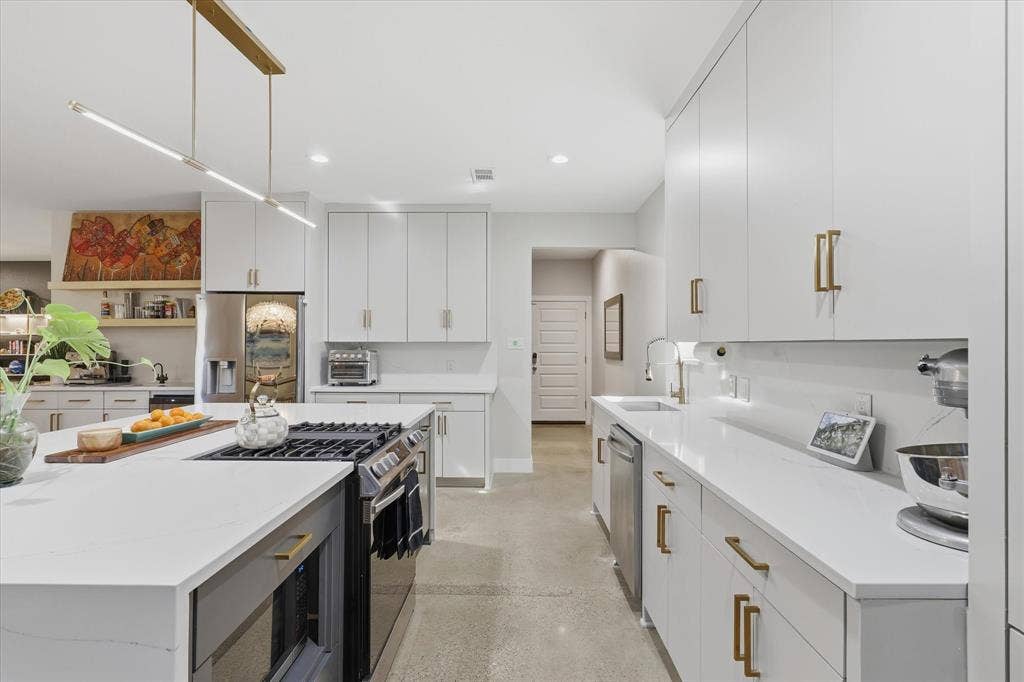 709 Woodbine Avenue, Dallas, TX 75203 Kitchen featuring a central island with a gas range, white cabinetry with gold-tone hardware, a stainless steel refrigerator, and a linear pendant light fixture