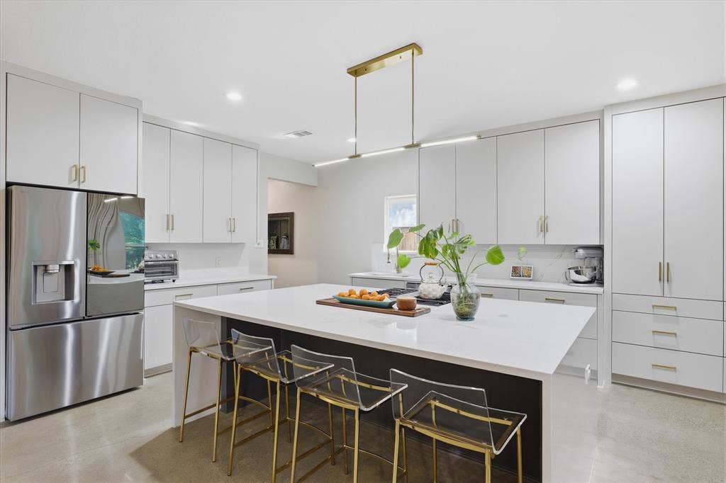 709 Woodbine Avenue, Dallas, TX 75203 White cabinetry with gold-tone hardware, stainless steel refrigerator, white countertops, kitchen island with seating, and a linear pendant light fixture
