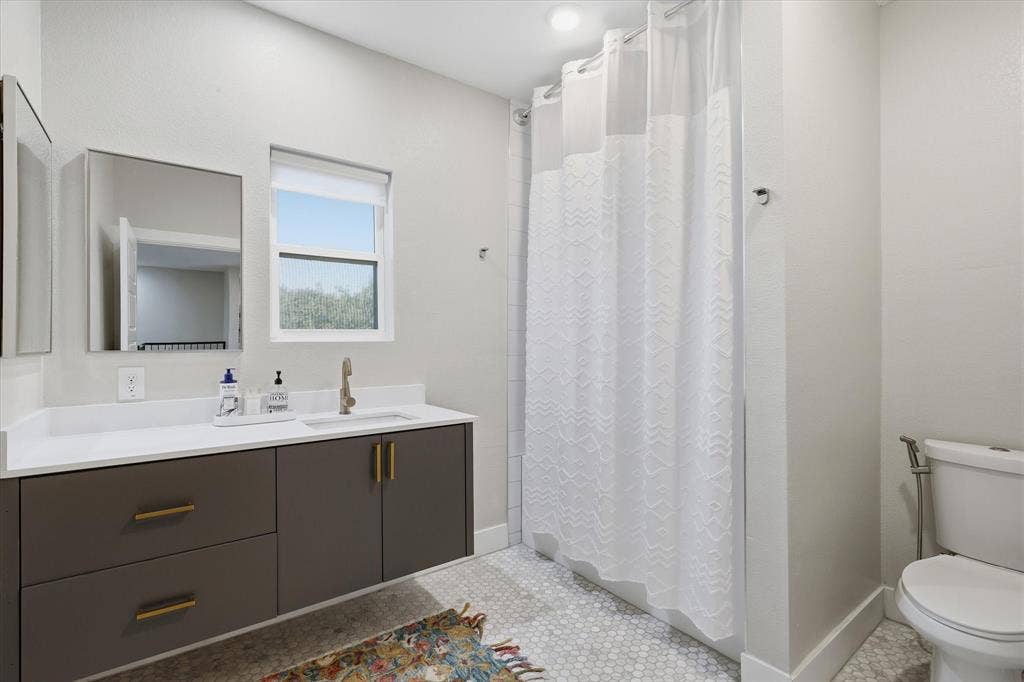 709 Woodbine Avenue, Dallas, TX 75203 White hexagonal tile flooring, vanity with brass hardware, large framed mirror, and a window for natural light