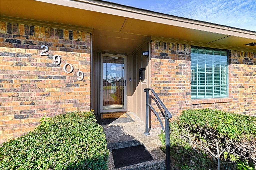 2909 Lee Park Drive, Irving, TX 75062 Multi-tonal brick exterior, covered entryway with concrete steps, metal handrail, and storm door with glass insert