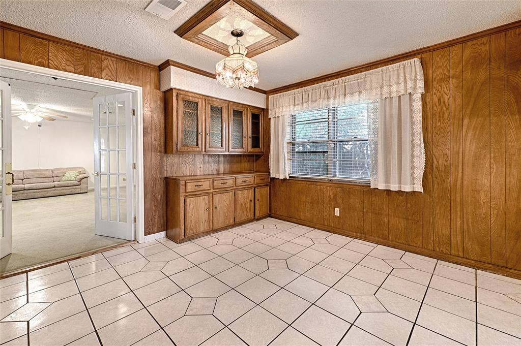 2909 Lee Park Drive, Irving, TX 75062 Wood-paneled walls, built-in wooden cabinetry with glass-front uppers, ceramic tile flooring, and a decorative ceiling-mounted chandelier