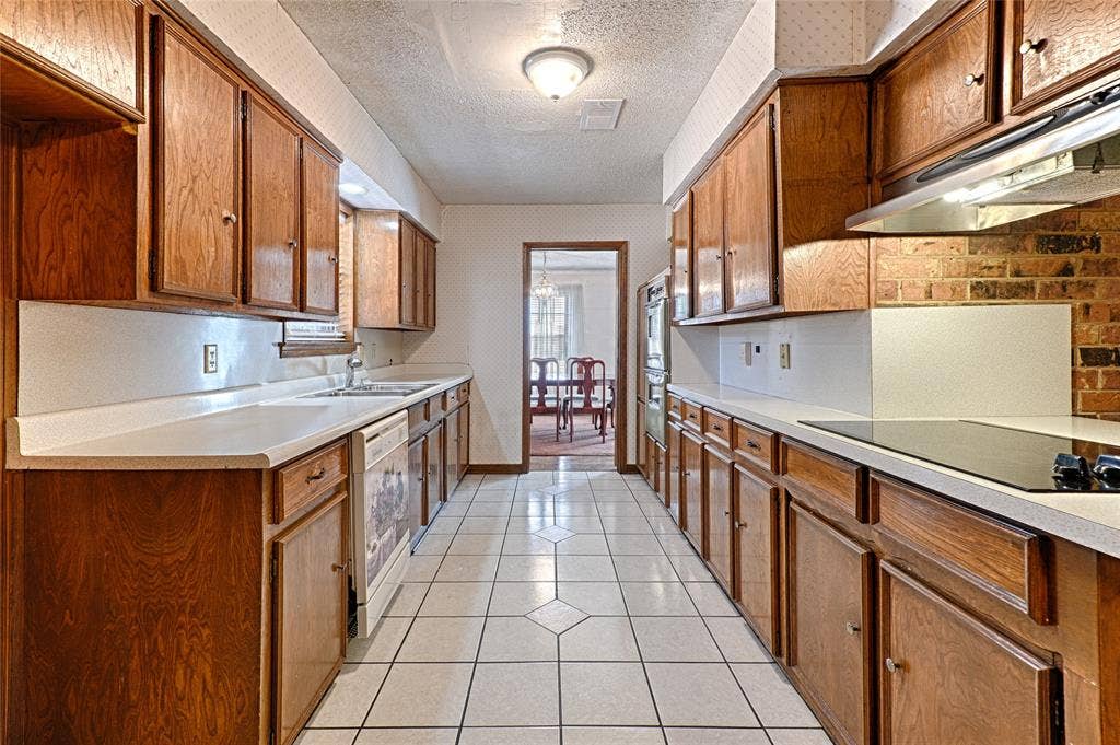 2909 Lee Park Drive, Irving, TX 75062 Galley kitchen featuring wood cabinetry, white solid-surface countertops, tile flooring, built-in wall oven, and a brick-accented cooktop surround