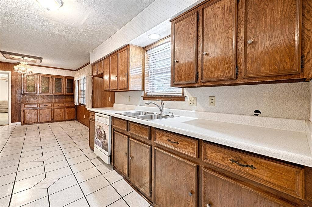2909 Lee Park Drive, Irving, TX 75062 Wood-finish cabinetry, white solid-surface countertops, dual-basin stainless steel sink, ceramic tile flooring, and integrated built-in storage hutch