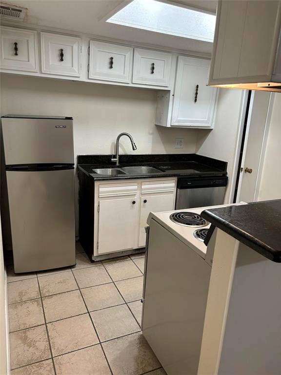 Kitchen with stainless steel appliances, exhaust hood, white cabinetry, sink, and light tile floors
