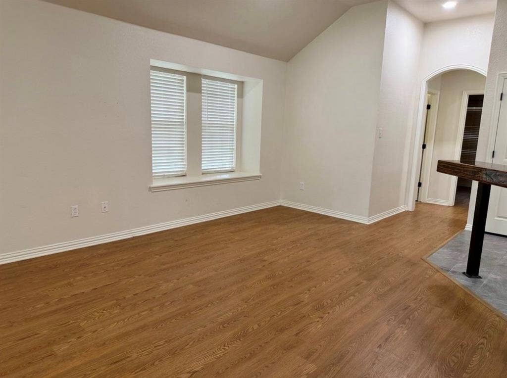 1001 Roberts Bend, Granbury, TX 76048 Vaulted ceiling, wood-finish flooring, two windows with blinds, arched doorway, and a built-in bar with a dark countertop