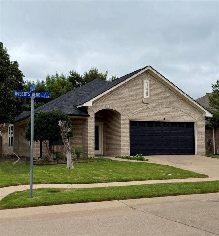 1001 Roberts Bend, Granbury, TX 76048 Light-toned brick exterior with an arched entry, dark garage door, and a dark shingle roof