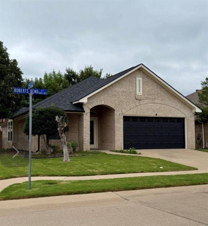 1001 Roberts Bend, Granbury, TX 76048 Cream brick exterior, arched entryway, dark asphalt shingle roof, two-car garage, and a concrete driveway