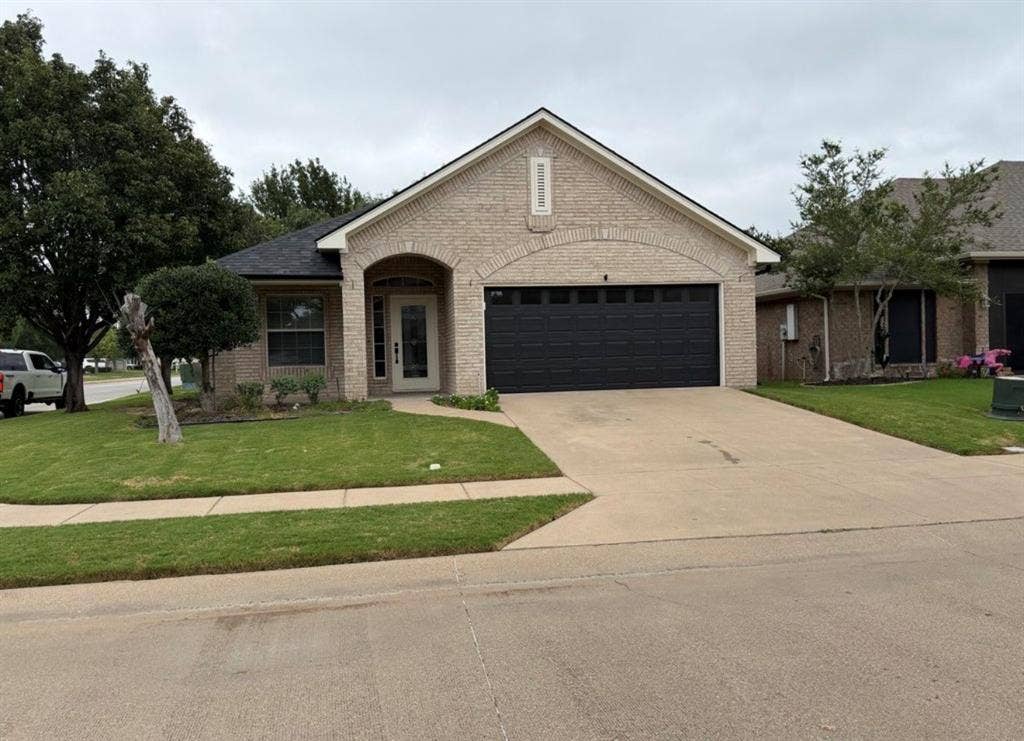 1001 Roberts Bend, Granbury, TX 76048 Light-colored brick exterior with an arched entryway, attached two-car garage, concrete driveway, and established front landscaping