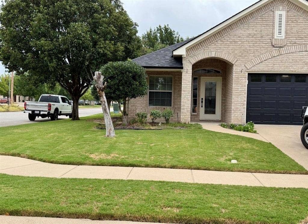 1001 Roberts Bend, Granbury, TX 76048 Light-toned brick exterior with an arched entry, black panel garage door, and a white decorative front door