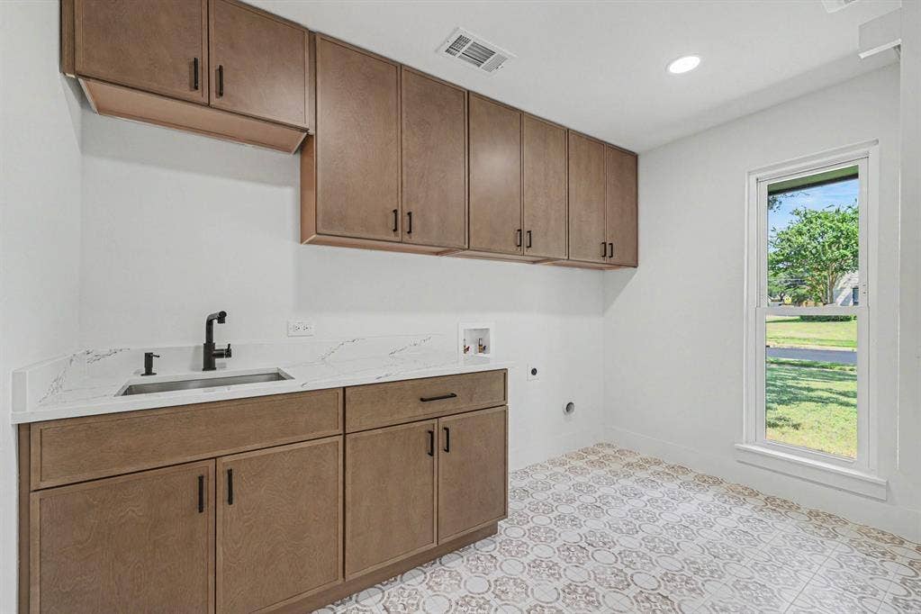 4004 Cedar Bayou Drive, Dallas, TX 75244 Functional utility room featuring extensive built-in cabinetry, a sink with a matte black faucet, light-toned countertops, and decorative floor tiling