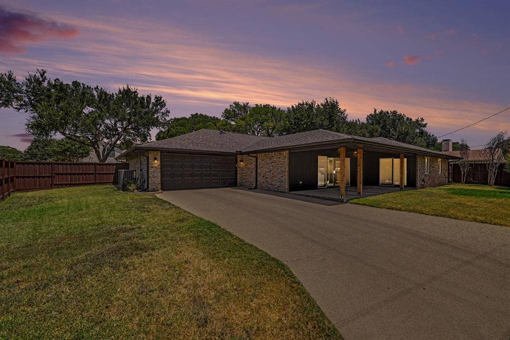 4004 Cedar Bayou Drive, Dallas, TX 75244 Brick facade with dark siding, covered patio with wooden columns, attached garage, paved driveway, and mature landscaping