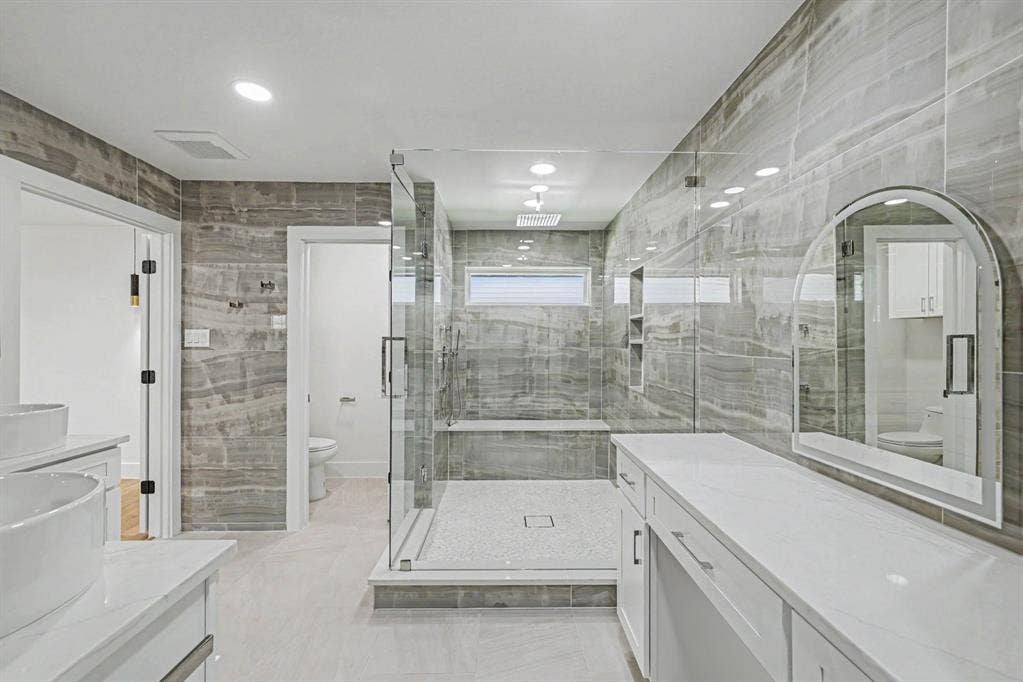4004 Cedar Bayou Drive, Dallas, TX 75244 Spacious bathroom with dual vanity sinks, extensive white cabinetry, large walk-in shower with glass enclosure, white countertop, and gray tiled walls