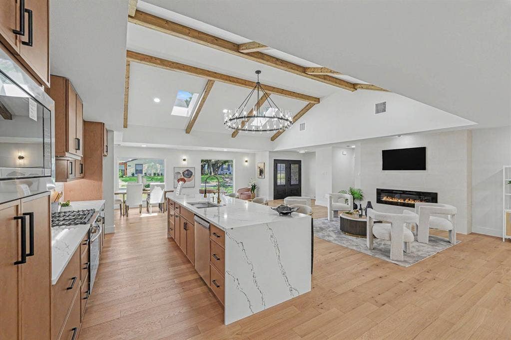 4004 Cedar Bayou Drive, Dallas, TX 75244 Vaulted ceilings with exposed wood beams, skylights, wood-finish flooring, a kitchen island with a waterfall countertop, and an integrated fireplace