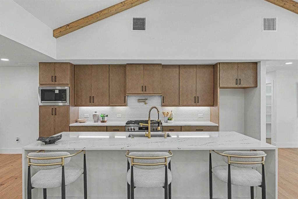 4004 Cedar Bayou Drive, Dallas, TX 75244 Vaulted ceiling with exposed wood beam, wood-finish cabinetry, white subway tile backsplash, white countertop island, and stainless steel appliances
