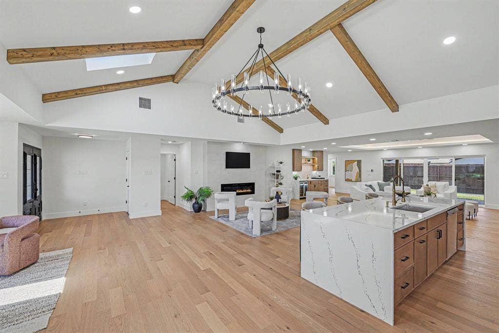 4004 Cedar Bayou Drive, Dallas, TX 75244 Vaulted ceiling with exposed wood beams, wood-finish flooring, central kitchen island with integrated sink, built-in fireplace, and sliding glass doors