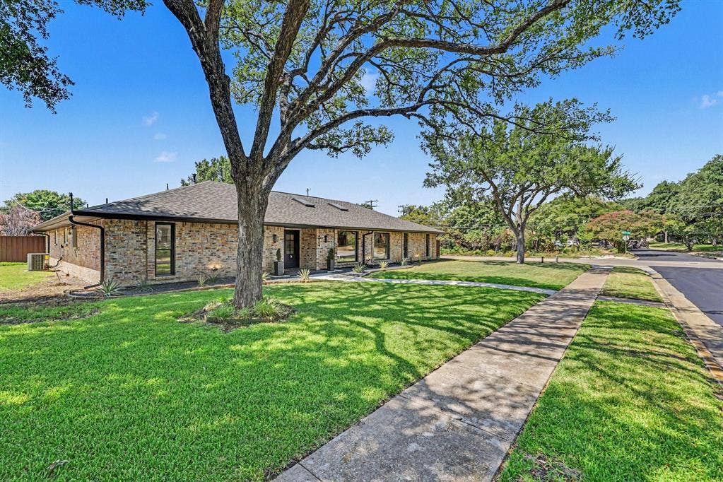 4004 Cedar Bayou Drive, Dallas, TX 75244 Brick exterior with a dark shingle roof, mature trees, concrete sidewalk, and manicured lawn