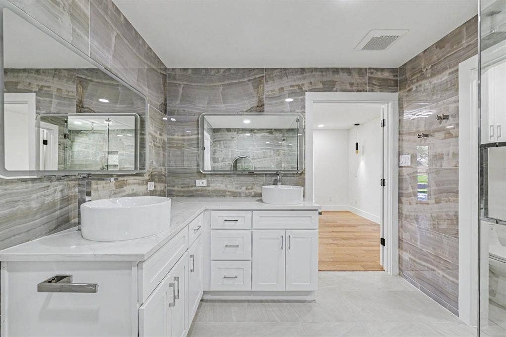 4004 Cedar Bayou Drive, Dallas, TX 75244 Dual vessel sinks with individual mirrors, custom white cabinetry, and stone-look wall tiling with coordinated flooring