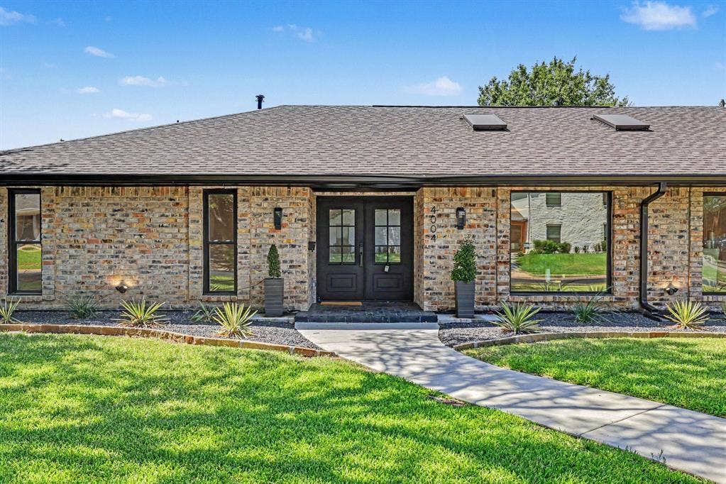 4004 Cedar Bayou Drive, Dallas, TX 75244 Brick exterior with dark-framed windows, double entry doors, and a shingle roof