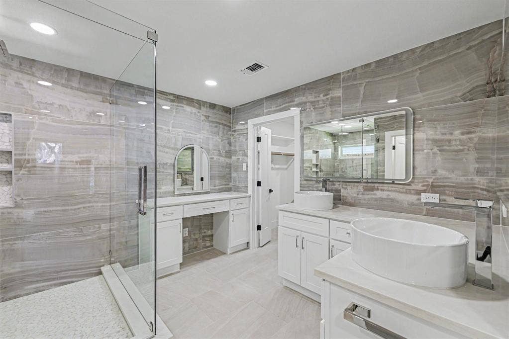 4004 Cedar Bayou Drive, Dallas, TX 75244 Spacious bathroom featuring a frameless glass shower enclosure, dual vessel sinks, extensive vanity cabinetry, a dedicated dressing vanity, and floor-to-ceiling stone-look wall tiling