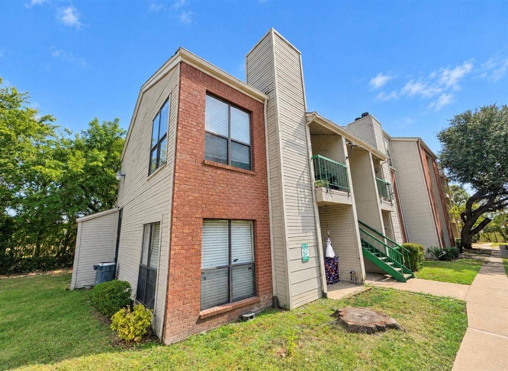 7126 Holly Hill Drive, #108, Dallas, TX 75231 Brick and siding exterior featuring multiple windows with blinds, a covered patio with green railings, an exterior staircase, and mature trees