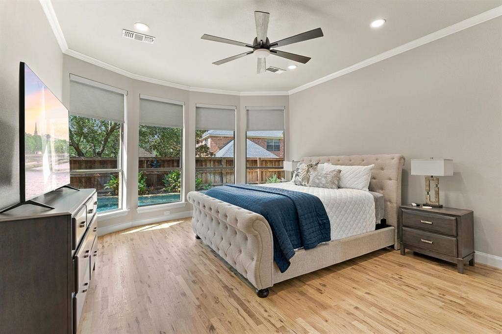 Primary Bedroom | Spacious main-level suite with wood flooring, recessed lighting, a ceiling fan and windows overlooking the pool.