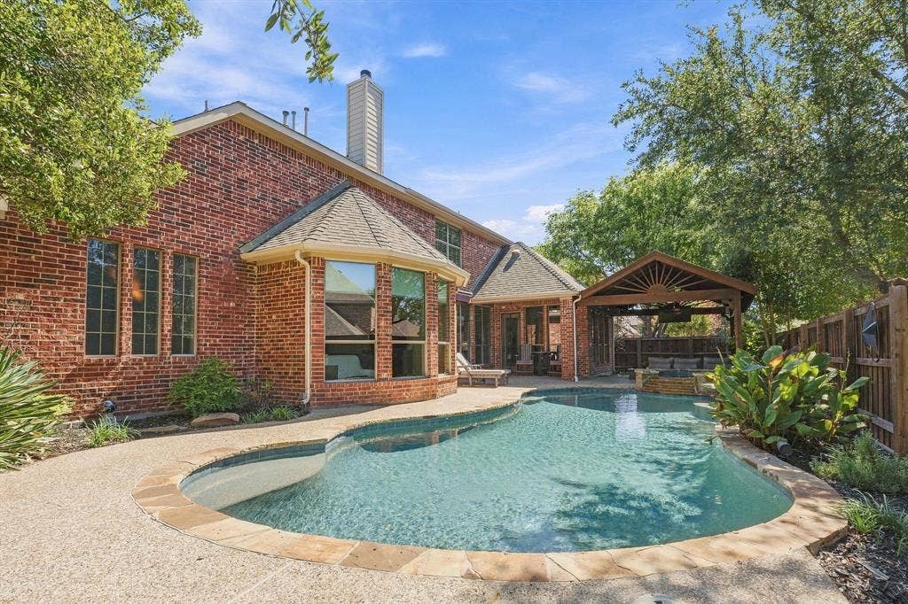 Rear Exterior and Pool | Wide view of the backyard retreat shows the pool, brick rear elevation and covered patio.