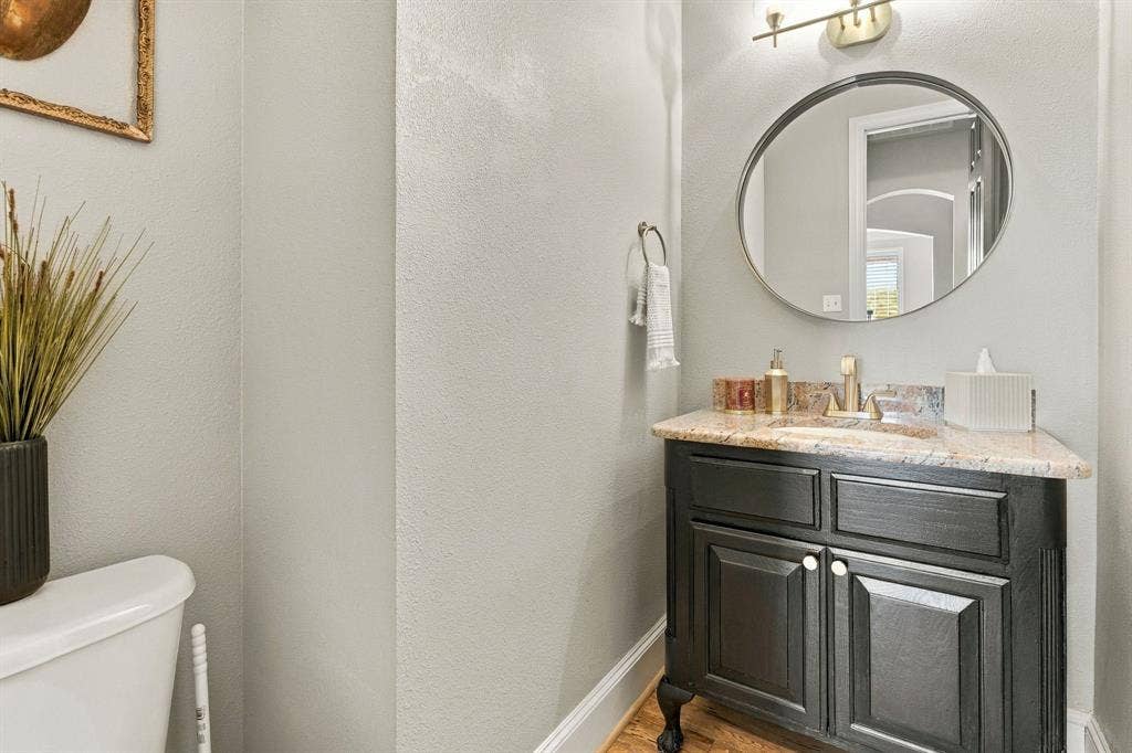 Powder Bathroom | Half bath with a furniture-style vanity, stone countertop and round mirror for main-level convenience.