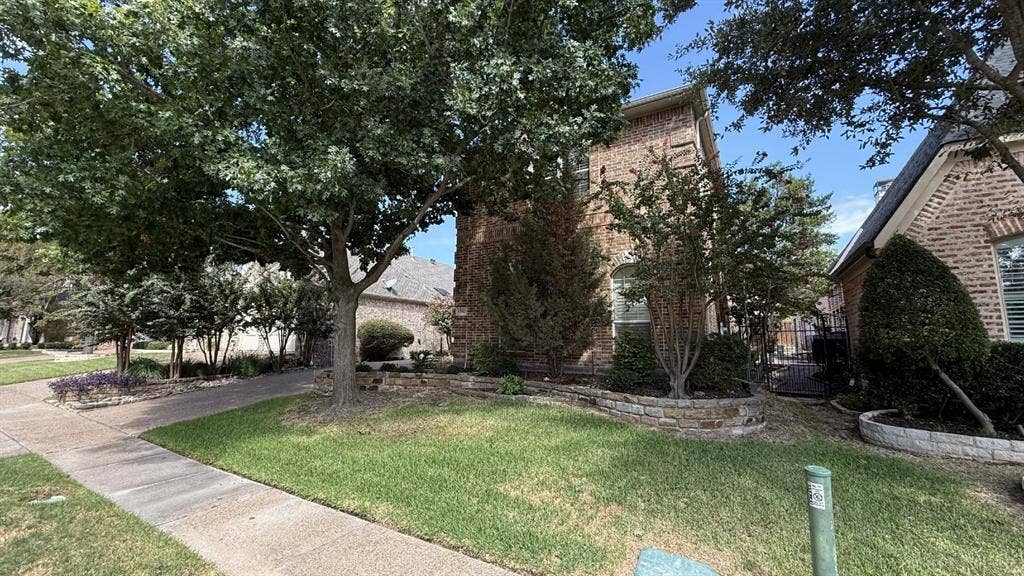 5700 Travis Drive, Frisco, TX 75034 Brick exterior with arched window, stone-finished retaining wall, and mature landscaping