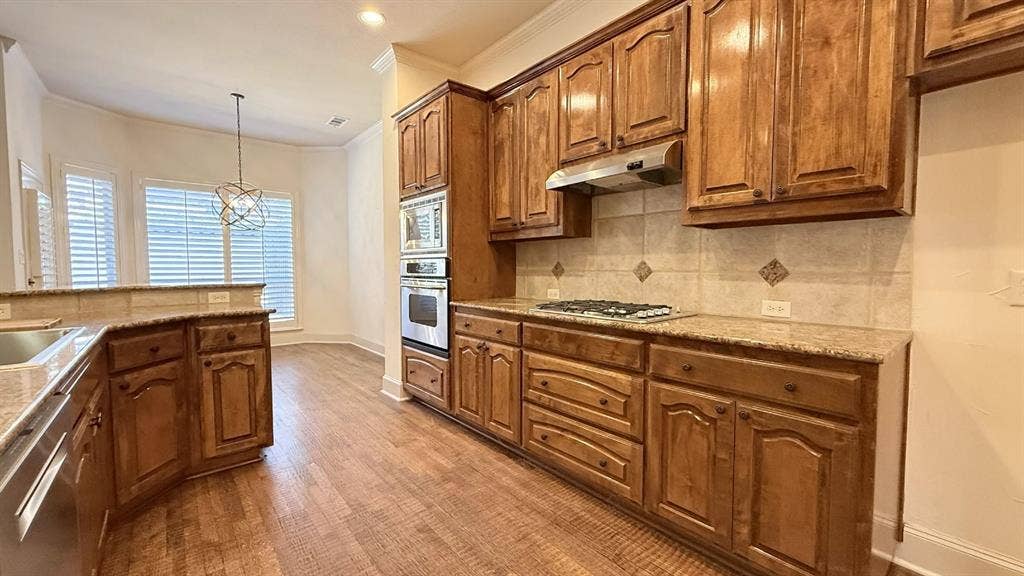 5700 Travis Drive, Frisco, TX 75034 Wood-finish flooring throughout, wood cabinetry, stone countertops, stainless steel appliances, and a tile backsplash