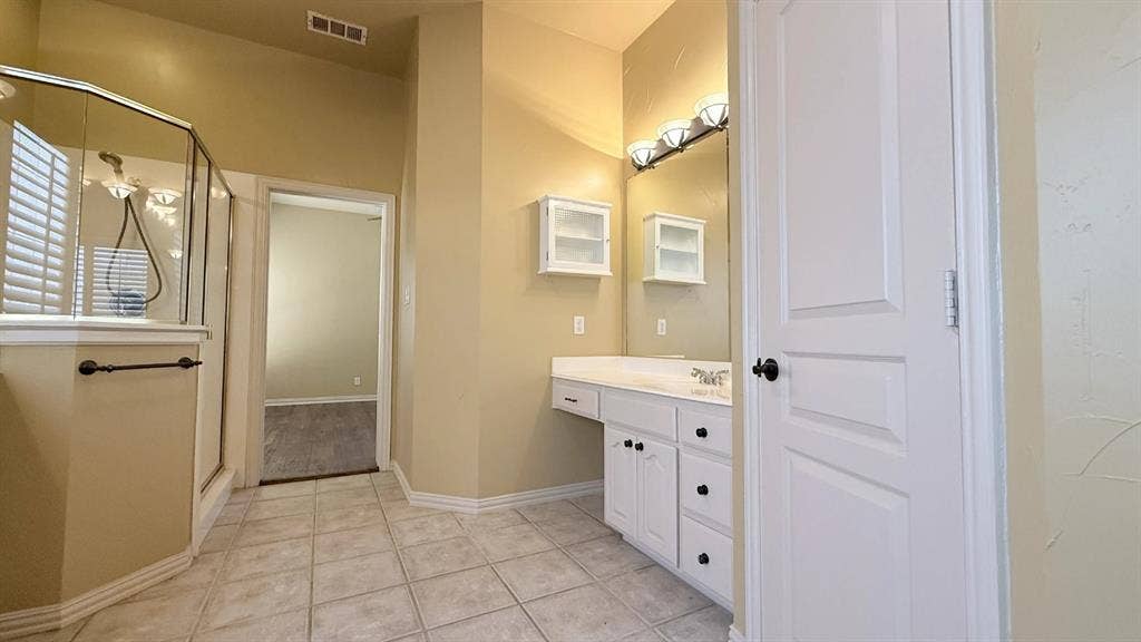 5700 Travis Drive, Frisco, TX 75034 Tiled flooring, glass-enclosed shower, white vanity with integrated sink, wall-mounted mirror, and white cabinetry