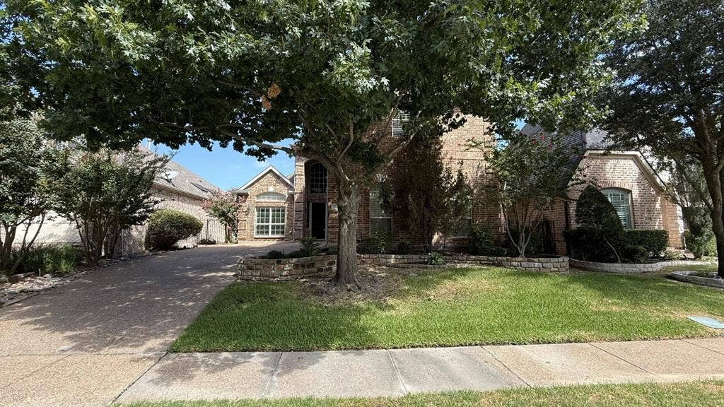 5700 Travis Drive, Frisco, TX 75034 Brick exterior with stone accents, arched entry, mature trees, and a concrete driveway
