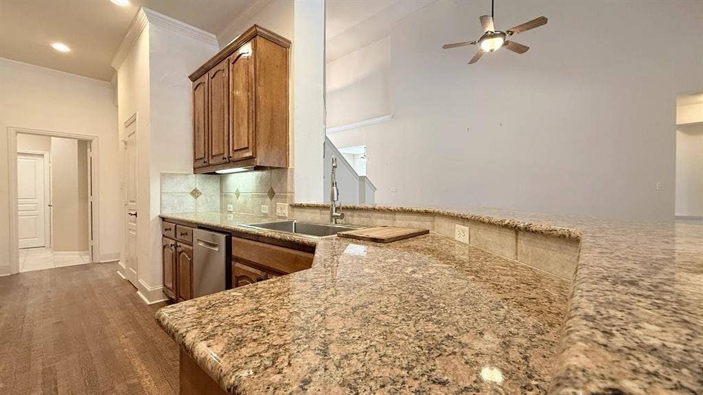 5700 Travis Drive, Frisco, TX 75034 Kitchen featuring granite countertops, wood-finish flooring, stainless steel dishwasher, wood cabinetry, and a tile backsplash