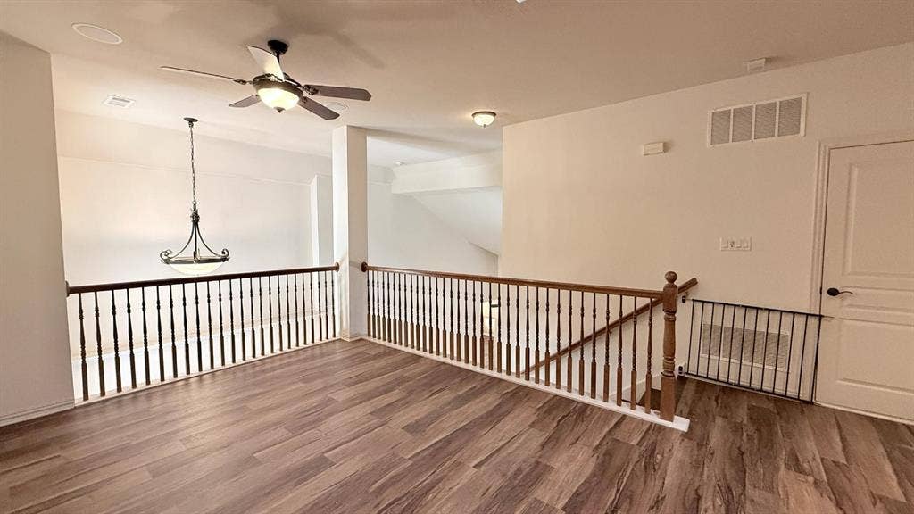 5700 Travis Drive, Frisco, TX 75034 Wood-finish flooring, white walls, dark wood balusters, a ceiling fan, and an overhead light fixture