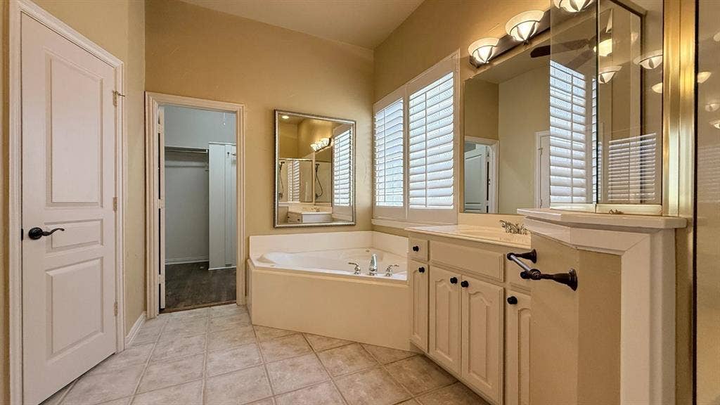 5700 Travis Drive, Frisco, TX 75034 Spacious bathroom featuring a corner soaking tub, dual vanity with cabinet storage, large mirror, and window with plantation shutters
