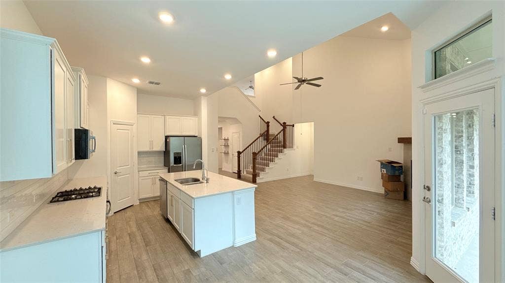 Open-concept living area with vaulted ceilings, wood-finish flooring, a contemporary ceiling fan, and a kitchen featuring white cabinetry, a central island, and stainless steel appliances