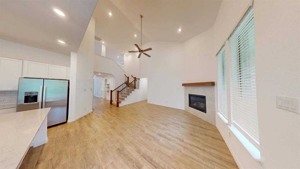 Vaulted ceiling, ceiling fan, wood-finish flooring, staircase with wood railing, and a fireplace with a wood mantle