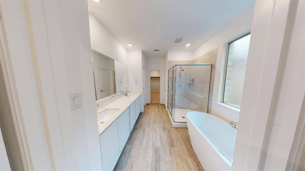 Dual vanity with rectangular undermount sinks, wood-finish flooring, glass-enclosed shower, freestanding soaking tub, and recessed lighting