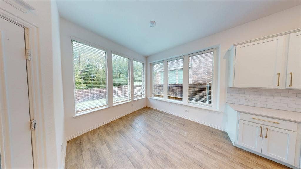 Wood-finish flooring, white cabinetry with gold-tone hardware, subway tile backsplash, and multiple windows